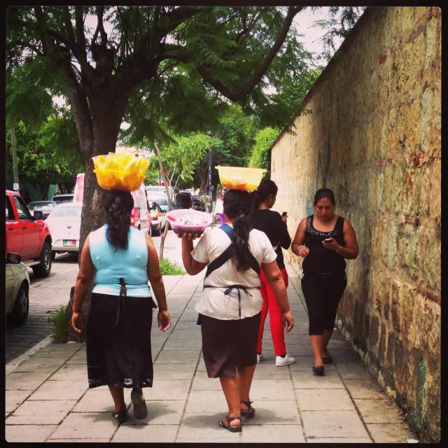 2 women with mangoes on head, other women with smartphones