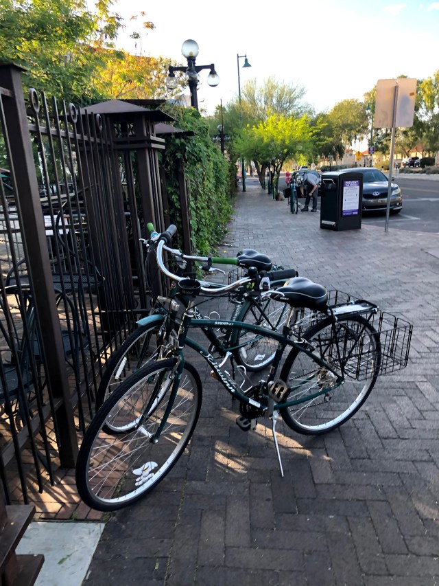2 green bikes with baskets, near a gate